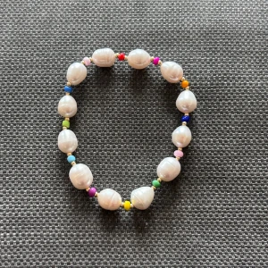 Färgglatt pärlarmband med sötvattenpärlor - Unikt armband med vita sötvattenpärlor och små färgglada pärlor i blått, rosa, rött, gult, grönt och lila. Armbandet har en lekfull och trendig stil som passar perfekt för dig som gillar att sticka ut med accessoarer. Elastisk tråd gör det enkelt att ta på och av.