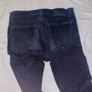 Mörkblå jeans från Nudie Jeans Co - Snygga mörkblå jeans från Nudie Jeans Co i klassisk femficksmodell. Jeansen är tillverkade i ekologisk bomull och har en rak passform med subtila slitningar och detaljerade bakfickor. Perfekta för dig som gillar stilrena och tidlösa jeans.