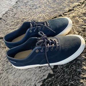 Mörkblå sneakers från Tommy Hilfiger - Snygga mörkblå sneakers från Tommy Hilfiger med vit sula och klassisk snörning. Ovandelen är i mocka och har diskreta logodetaljer på plösen och innersulan. Perfekta för en stilren och avslappnad look.