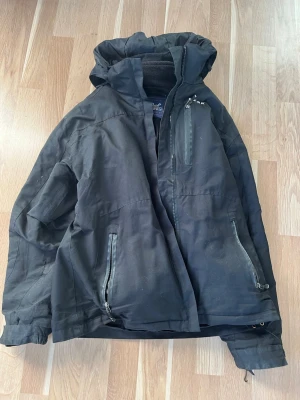 Svart vindjacka Peak Performance L - Svart vindjacka från Peak Performance i storlek L. Jackan har huva, flera dragkedjeförsedda fickor och meshfoder på insidan. Perfekt för blåsiga dagar och outdoor-aktiviteter. Snygg och funktionell design med justerbara detaljer.