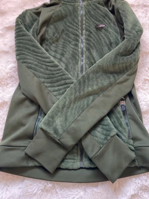 Grön fleecejacka från JH Collection - Mysig grön fleecejacka från JH Collection med hel dragkedja framtill och två sidofickor med dragkedja. Jackan har långärmad design och är tillverkad i mjuk fleece som håller dig varm under kyliga dagar. Perfekt för lager på lager under höst och vinter. Pris 40kr