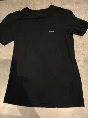 Svart BOSS t-shirt i bomull - Snygg svart t-shirt från BOSS med diskret logga broderad på bröstet. Klassisk rund halsringning och korta ärmar. Tillverkad i mjuk bomull som känns skön mot huden. Perfekt till jeans eller shorts för en clean look.