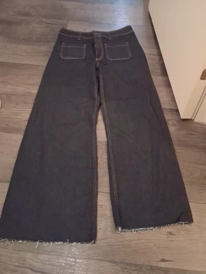 Wide jeans från Zara, mörkblå, strl 42 - Mörkblå jeans från Zara i storlek 42 med breda ben och råa, fransiga benslut. Klassisk femficksmodell med kontrastsömmar och hög midja. Snyggt retroinspirerat snitt som ger en avslappnad vibe. Perfekta till sneakers eller boots.