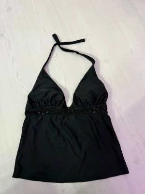 Svart halterneck linnetopp med broderi - Säljer en svart halterneck linnetopp med djup v-ringning och knyt i nacken. Toppen har fina broderade detaljer och små svarta pärlor under bysten. Materialet känns mjukt och lätt, perfekt för varma dagar. Vet ej vart den är köpt! I mycker bra skick!