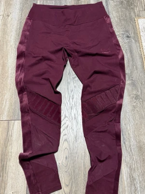 Vinröda leggings från Puma x Kenza - Snygga vinröda leggings från Puma x Kenza med bred resår i midjan och sammetsdetaljer längs sidorna. Stora PUMA-loggor i sammet på benen och diskret broderad logga vid höften. Stretchigt material som sitter skönt och följer kroppen. OBS: mindre i storlek, skulle säga att dessa passar S 
