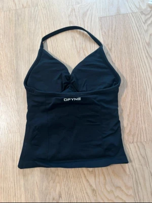 Svart halterneck linnetopp - Säljer en svart linnetopp  med halterneck och lätt rynkad detalj vid bysten. Toppen är ärmlös och har en tight passform som framhäver figuren. 