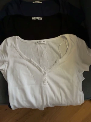 3-pack toppar Terranova XS - Säljer tre basic toppar från Terranova i storlek XS. En vit, en svart och en marinblå, alla med kort ärm, v-ringning och knappar framtill. Tillverkade i mjuk bomull,knappt använda och perfekta att matcha till olika outfits. Köpta i italien och säljs då de inte är min stil längre❤️