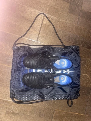 Nike Tiempo 10 - Fotbollskor Nike tiempo 10 Elite i färg blå och svart. Jag har använt skorna i en säsong det är inga större defekter som jag märkt av varken på planen eller hur dem ser ut förutom att dobbarna är lite nedtrampade. Förutom skorna får du även med en skopåse som matchar med skorna. OBS! Skorna är 39 och inte 38 plick hade inte det som val. Skriv om det skulle vara någon fråga 