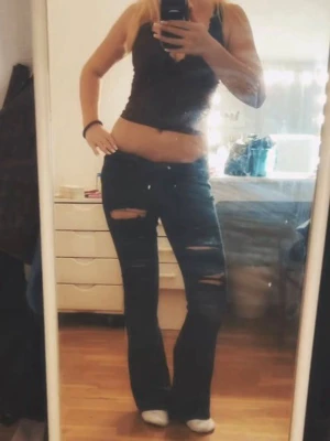 Bootcut jeans med slitningar - Säljer ett par mörkblå bootcut jeans med slitna detaljer på låren och knäna. Byxorna har låg midja och klassisk femficksdesign. Perfekta för dig som gillar en avslappnad och trendig stil.