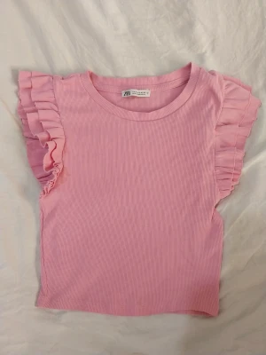 Rosa ribbad topp med volang från Zara - Rosa ribbad top med volangärmar från Zara i storlek S. Inga fläckar och i bra skick. Katt finns i hemmet.  