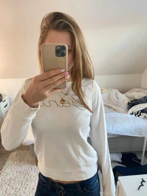 Vit sweatshirt från Gant med guldtext - Säljer en fräsch vit sweatshirt från Gant med snyggt broderad guldig text på bröstet. Tröjan har rund hals, ribbade muddar och är långärmad. 