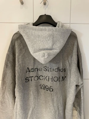Acne hoodie  - Grå hoodie från Acne Studios med tryck på ryggen (Stockholm 1996). Använd i gott skick, storlek L. Klassisk passform och mjuk kvalitet. Köpbevis finns – skriv till mig så skickar jag köpbeviset.