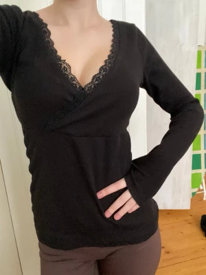 Svart omlottopp med spets från Anna Field - Svart långärmad omlottopp från Anna Field med v-ringning och fina spetsdetaljer längs urringningen. Storlek M (passar XS-M)