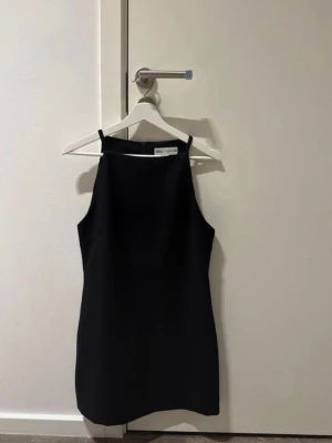 Svart kort klänning  - Stilren svart klänning från ZARA med rak passform och smala axelband. Klänningen är kort och har en enkel design! Använd ett fåtal gånger!