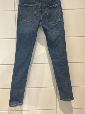 Blå slim jeans med slitningar - Säljer ett par blå slim jeans med snygga slitningar och klassiska fem fickor. Jeansen har en smal passform och normal midja, perfekta till sneakers eller boots. Materialet är mjukt jeans-tyg som sitter tajt men ändå bekvämt.