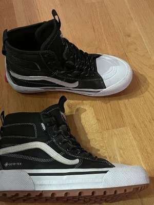 Svarta Vans Gore-Tex boots MTE - Säljer ett par svarta Vans MTE boots med vit sula och tå, tillverkade i slitstark Gore-Tex och syntet. Skorna har grov mönstrad sula för grymt grepp, snörning och klassisk vit Vans-stripe på sidan. Perfekta för kalla och blöta dagar. Använda endast ett fåtal gånger förra vintern och är nu för små i storlek.