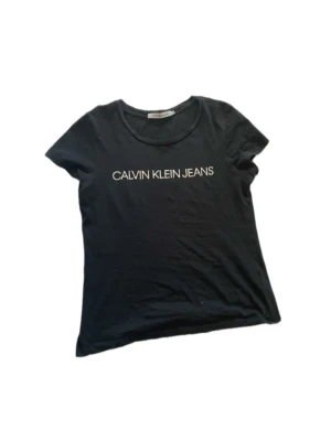 Svart Calvin Klein Jeans t-shirt - Snygg svart t-shirt från Calvin Klein Jeans med klassisk logga tryckt i vitt framtill. Den passar sin figur väldigt bra, med korta armar. Säljer pgv att jag inte använder.