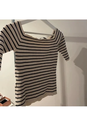 Randig ribbad topp offshoulder - Säljer en ribbad topp med svart och vit randigt mönster. Toppen har offshoulder-modell och korta ärmar, samt en fyrkantig urringning. Materialet är stretchigt och sitter snyggt på kroppen. Perfekt till jeans eller kjol för en trendig look.
