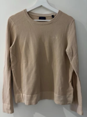 Beige stickad tröja från GANT - Säljer en stilren beige stickad tröja från GANT i storlek S. Tröjan har rund halsringning, lång ärm och diskret gant logga i materialet. 