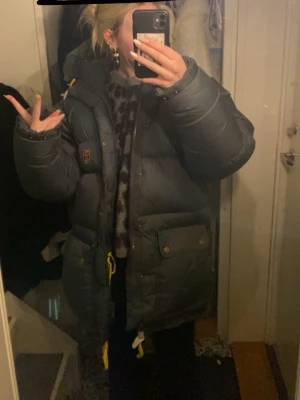 Mörkgrå dunjacka från Fjällräven kan tänka  byta mot en mindre storlek - Säljer en mörkgrå dunjacka från Fjällräven med gul snörning och stora fickor framtill. Jackan har en hög krage och huva, perfekt för kalla dagar. Klassisk Fjällräven-logga på bröstet och praktiska detaljer som dragkedja och knappar. Storlek s men passar som M/L mer det är den gamla modellen 