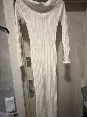 Vit ribbad långklänning - Säljer en superfin långklänning i ribbad vit trikå med lång ärm och bred, nedvikt krage. Klänningen har en tight passform som framhäver figuren och är perfekt för dig som gillar minimalistisk stil.