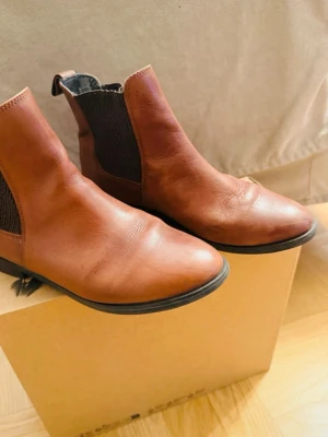 Bruna chelsea boots i skinn - Snygga bruna chelsea boots i skinn med elastiska partier på sidorna och dragflik bak. Skorna har rund tå och platt sula, perfekta till jeans eller kjol. Klassisk modell som funkar året runt och ger en stilren look. XIT Din Sko
