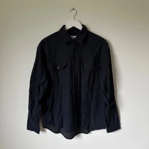 Mörkblå overshirt från Selected Homme - Mörkblå overshirt från Selected Homme i mjuk bomull, med klassisk krage och två stora bröstfickor med knappar. Långärmad modell med knappstängning framtill och på ärmsluten. Perfekt för en hoodie under och enkelt att stylea sommar som vinter