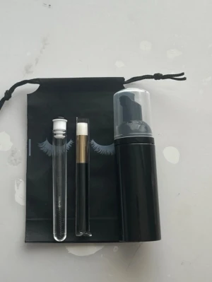 Kit för ögonfransrengöring till Fransförlängning - Snyggt kit med svart rengöringsflaska, vit borste med svart och guld handtag samt ett genomskinligt rör med vit kork. Perfekt för att rengöra och vårda ögonfransarna. Kommer med svart påse med snörning och fransmotiv. Fransschampo 