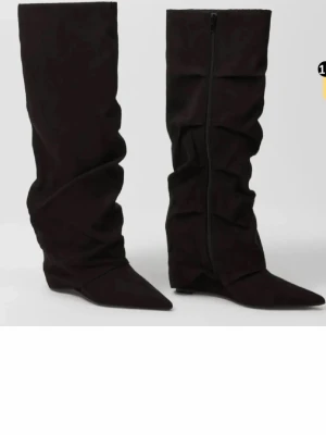 Nelly svarta boots - Säljer ett par svarta stövlar med snyggt rynkad design och spetsig tå. Stövlarna har en platt sula och är tillverkade i mocka för en mjuk och lyxig känsla. Perfekt för dig som vill ha en cool och trendig look.