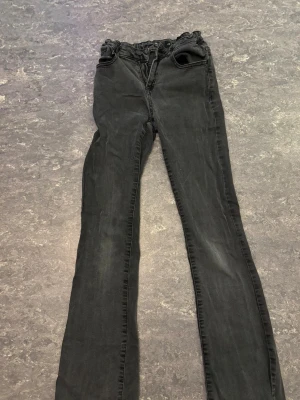 Svarta bootcut jeans  - Snygga svarta jeans med bootcut passform och snörning i midjan. Modellen har klassiska fickor fram och bak samt en något högre midja. Materialet är mjukt och stretchigt jeans, perfekt för en cool och avslappnad look.
