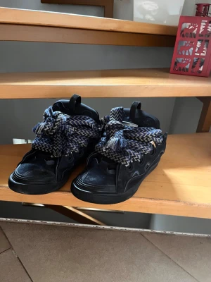 Lanvin curb - Unika svarta sneakers i storlek 45 med chunky design och rund tå. Skorna har extra breda snören i blått, vitt och grått zigzag-mönster som ger en cool touch. Tillverkade i Portugal med detaljer i syntet och mocka. Perfekta för dig som gillar statement-skor.