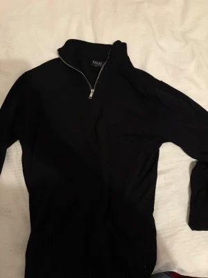 Svart stickad half zip-tröja MAN - Svart stickad tröja från MAN med half zip-dragkedja i halsen. Klassisk modell med långärmad passform och hög krage. Perfekt för dig som gillar stilrena och enkla plagg med lite edge. Snygg att matcha med jeans eller chinos.