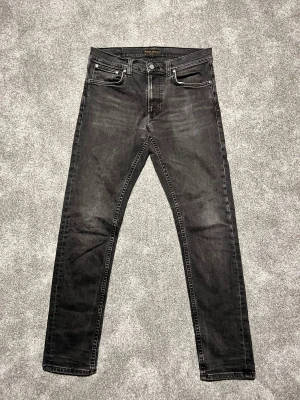 Svarta slim jeans från Nudie Jeans W31 L32 - Snygga svarta jeans från Nudie Jeans med slim passform och klassisk femficksdesign. Jeansen har en mörk tvätt med subtila slitningar och kontrastsömmar. Materialet är mjukt och stretchigt denim för skön komfort. Perfekt för dig som gillar en smal siluett.Dem är lagade från Nudie dem själva.Lagade från Nudie Jeans.