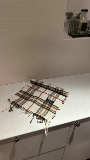 Rutig ullväst från Burberrys - Snygg rutig väst från Burberrys i klassiskt beige, svart, vit och röd färg. Västen är tillverkad i 100% lammull och har fransade kanter. Den ikoniska Burberry-rutan ger en tidlös vibe och passar perfekt till lager-på-lager-stil.