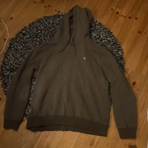 Brun hoodie från Morris med huva - Säljer en brun hoodie från Morris med huva och snörning. Tröjan har en liten broderad logga på bröstet och en patch nertill. Mjuk insida och klassisk passform, perfekt för chill dagar. Storlek S.