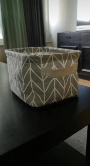 Grå tygkorg med vitt mönster - Snygg grå tygkorg med vitt grafiskt mönster. Korgen är rektangulär och har ett praktiskt handtag på kortsidan. Perfekt för att organisera småsaker i rummet. Korgen går att trycka ihop. Korgen är ca 20x16 cm med ett djup på ca 14 cm