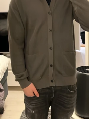 Grön kofta från Massimo Dutti - Snygg grön kofta från Massimo Dutti i 100% bomull. Den har en klassisk krage, knappar hela vägen och två stora fickor framtill. Passformen är normal och ärmarna är långa. Perfekt för dig som gillar stilrena och enkla plagg. Använd cirka två gånger så det är nästan helt ny