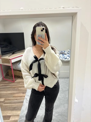 Vit stickad cardigan med svarta rosetter - Superfin vit stickad kofta med två stora svarta rosetter framtill. Endast använd 1 gång🥰🤍