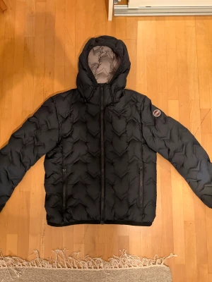 Colmar pufferjacka  - Säljer en svart pufferjacka från Colmar med snyggt quiltat mönster och huva. Jackan köptes på Zalando för ungefär 5 000kr ny, den är knappt använd och har inga skador alls, storlek 50 alltså M, jag är 188 (på bilden).