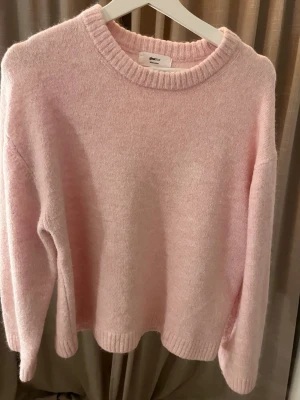 Ljusrosa stickad tröja Gina Tricot - Supermysig ljusrosa stickad tröja från Gina Tricot i ullblandning. Tröjan har rund hals, ribbade muddar och långärmad passform. Perfekt för dig som gillar en chill och enkel stil med lite extra cozy-vibe.