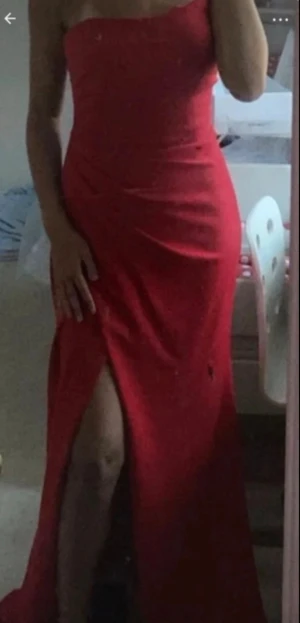 Röd balklänning med slits - Säljer en snygg röd långklänning med axelbandslös design och hög slits framtill. Klänningen har en figurnära passform och lätt drapering över bysten. Perfekt för dig som vill sticka ut med en klassisk och elegant look.