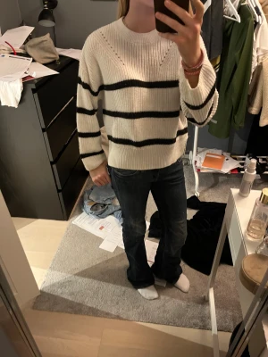 Vit och svart randig stickad tröja - Säljer en mysig stickad tröja i vit med svarta breda ränder. Tröjan har rund hals, långärmade ärmar och ribbade muddar. 