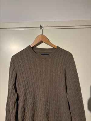 Brun kabelstickad tröja Bondelid S - Snygg brun kabelstickad tröja från Bondelid i storlek S. Tröjan har rund hals och ett klassiskt flätmönster över hela plagget. Perfekt för dig som gillar stilrena och tidlösa plagg med lite extra struktur. Passar dig som vill ha en chill och enkel look.