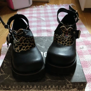 Svarta platåskor från Demonia med leopardmönster - Jätte Snygga svarta platåskor från Demonia med leopardmönstrad insida som är använda en gång då jag fick dom som present men fick ingen mer andvänding av dom . Skorna har också justerbara remmar med spännen, kvar i boxen❤️
