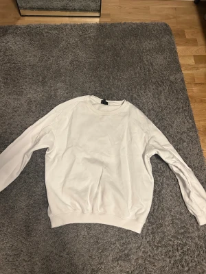 Vit sweatshirt från H&M Relaxed Fit M - Enkel och clean vit sweatshirt från H&M i relaxed fit. Tröjan har rund halsringning, ribbade muddar och är tillverkad i mjuk bomullsblandning. Perfekt för dig som gillar en avslappnad och stilren look.