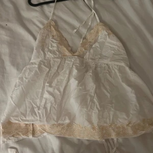 Vit broderad linnetopp från ASOS - Supersöt vit linnetopp från ASOS med tunna axelband som knyts i nacken. Toppen har broderade detaljer i ljusgul färg längs v-ringningen och nederkanten. Nyskick.