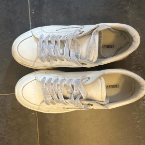 Zadig and voltarie sneakers med rosa detalj - Snygga vita sneakers från Zadig & Voltaire med glittriga vita skosnören och en rosa detalj på hälen. Använda cirka 2 gånger. Nypris 2000kr men säljer billigt för har så många skor.