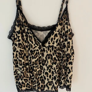 Leopardmönstrad linnetopp med spets - Snygg linnetopp med leopardmönster i beige och svart, med svarta spetsdetaljer längs kanterna. Smala justerbara axelband och v-ringning.