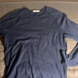 Blå stickad tröja från J.Lindeberg - Mysig blå stickad tröja från J.Lindeberg med rund halsringning och långa ärmar. Perfekt för lager-på-lager och enkel att matcha med jeans eller chinos. Klassisk och stilren design som funkar året runt.