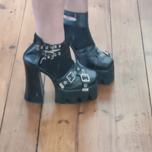 Svarta platåskor med spännen - Säljer ett par coola svarta platåskor i syntetmaterial. De har flera spännen och dragkedja bak för en edgy look. Perfekta för en utekväll eller fest! Skorna har en rejäl klack som är super hög! For my alts and emos out there!